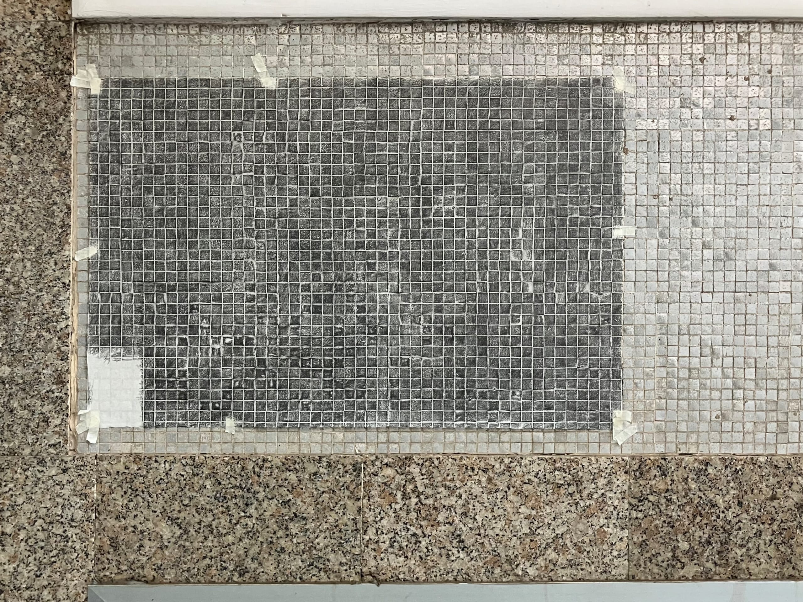 Papel japonés fijado sobre un revestimiento de teselas cuadradas, con un frottage en grafito que reproduce una retícula irregular de cuadrados oscuros.